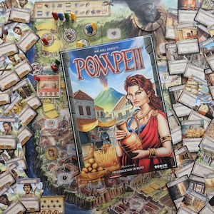 May include: The board game "Pompeii" is displayed, featuring a cover illustration of a woman with a jug, set against a volcanic eruption and ancient city. Cards and game pieces surround the game board.