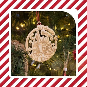 May include: A wooden Christmas ornament with the words "Welcome to Hogwarts" cut out. The ornament features a detailed depiction of a castle and is hanging on a Christmas tree. The ornament is round and has a red string for hanging.