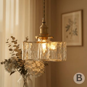 May include: A retro pendant light with a textured, rectangular glass shade. The light fitting has a brass-coloured metal base and a single bulb. The image shows the light fitting suspended from a cord, emitting a soft, warm glow.