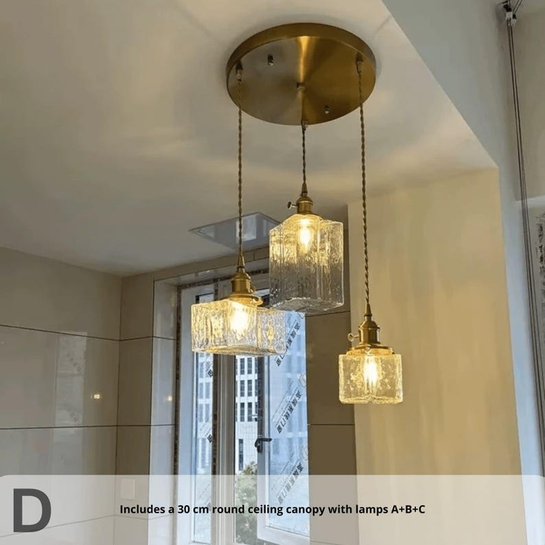 May include: Three pendant lights with textured glass shades and brass-coloured hardware hang from a circular ceiling canopy. The lights are suspended by twisted cords. The text in the image says "Includes a 30 cm round ceiling canopy with lamps A+B+C."