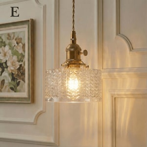 May include: A vintage-style pendant light with a clear, textured glass shade and brass-colored hardware. The shade has a geometric pattern, and the light bulb is visible. The fixture hangs from a twisted brown cord.