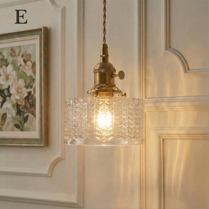 May include: A vintage-style pendant light with a clear, textured glass shade and brass-colored hardware. The shade has a geometric pattern, and the light bulb is visible. The fixture hangs from a twisted brown cord.