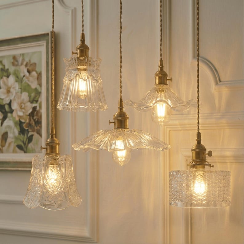 May include: Five vintage-style pendant lights with clear glass shades and brass fixtures hang from the ceiling. The shades have various designs, including floral patterns and textured surfaces, and are illuminated by warm-toned bulbs.