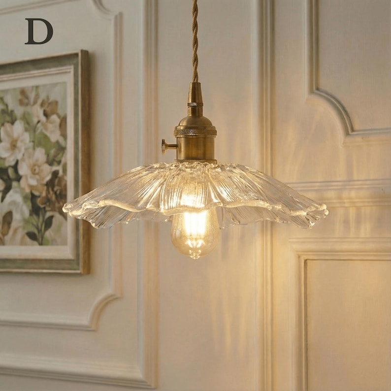 May include: A vintage-style pendant light with a clear, ruffled glass shade and a brass-colored fixture. The light bulb is visible, emitting a warm glow. The fixture hangs from a twisted brown cord. The letter "D" is in the upper left corner.