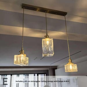 May include: Three-light pendant fitting with rectangular, textured glass shades and brass-toned hardware. Includes a 60 cm rectangular ceiling canopy. The lights hang from twisted cords.