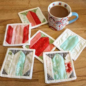 May include: Six handmade fabric coasters with a white border. The coasters feature a variety of patterns in red, pink, green, and white.