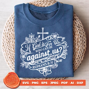 Op de afbeelding: Een blauw T-shirt met een wit ontwerp met een kruis, bloemen en de tekst "Als God voor ons is, wie kan dan tegen ons zijn? Romeinen 8:31".