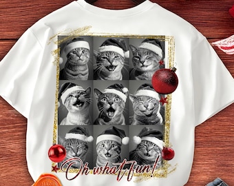 Puede incluir: Camiseta blanca con una cuadrícula de nueve retratos de gatos en blanco y negro con gorros de Papá Noel. La frase "Oh what fun!" está escrita en cursiva. Adornos navideños rojos y un marco dorado brillante añaden toques festivos.