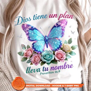 May include: White t-shirt featuring a large butterfly with blue and purple wings, surrounded by pink, blue, and cream roses. The shirt has the text "Dios tiene un plan" and "lleva tu nombre" with a Bible verse reference. A digital download graphic.