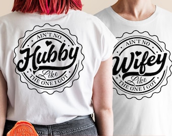 May include: White t-shirts with black text that reads "Ain't No Hubby Like The One I Got" and "Ain't No Wifey Like The One I Got" in a circular design. The shirts are for couples.