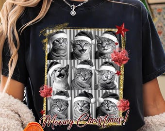 Puede incluir: Camiseta negra con una cuadrícula de nueve gatos con gorros de Papá Noel y el texto "Meowy Christmas!". El diseño incluye estrellas rojas brillantes y un marco dorado. Un diseño festivo para la temporada navideña.
