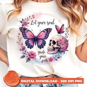 Puede incluir: Una camiseta blanca con una mariposa rosa, una calavera y flores. El texto "Let your soul guide your path" está impreso en la camiseta.