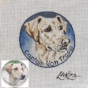 May include: A needlepoint canvas with a round image of a yellow Labrador Retriever's head. The dog's name, "Captain Von Trapp", is written in a blue circle around the dog's head. The artist's signature, "Lunza", is written in the bottom right corner of the canvas.