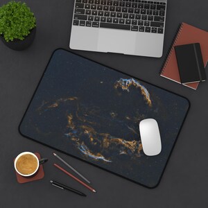 Op de afbeelding: Een zwarte muismat met een galaxy-achtig ontwerp met draaiende blauwe en oranje tinten. Een witte computermuis ligt op de mat.
