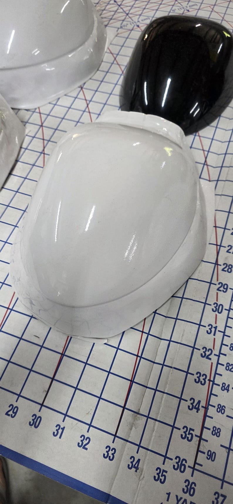 Pu&ograve; includere: Caschi bianchi e neri disposti su una superficie a griglia. Il casco bianco &egrave; in primo piano, con una finitura lucida. L'immagine mostra un primo piano dei caschi.