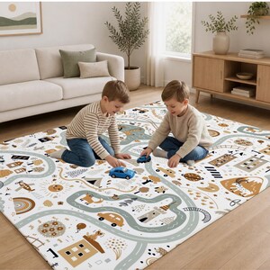 May include: A rectangular area rug featuring a white background with a printed pattern of winding gray roads, brown houses, trees, animals, rainbows, and suns. The rug displays a playful map design with various illustrations of buildings and nature.