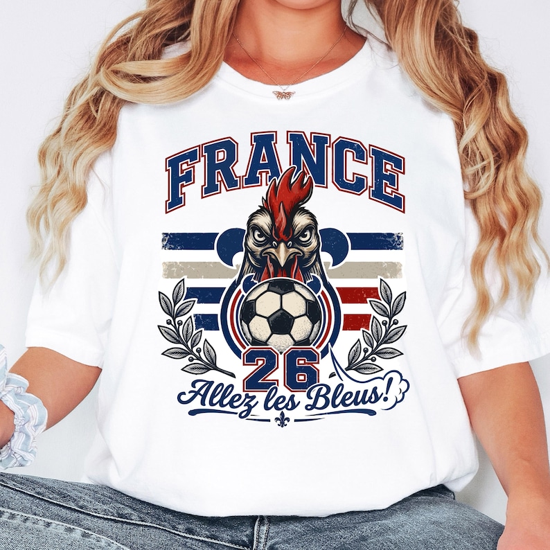 May include: White t-shirt featuring a graphic of a rooster with a soccer ball, the word "FRANCE" in blue, and the text "Allez les Bleus!" in blue. The design incorporates the colors red, white, and blue, with a distressed vintage style.