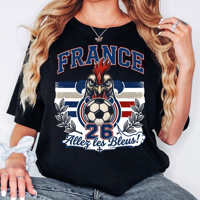 May include: Black t-shirt with a graphic featuring the word "FRANCE" in blue and white, a rooster with a soccer ball, and the text "26 Allez les Bleus!". The design incorporates the colors of the French flag.