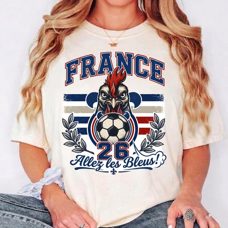 May include: Cream-colored t-shirt featuring a graphic of a rooster with a soccer ball, the word "FRANCE" in blue, and the text "Allez les Bleus!" in black. The number "26" is also displayed. The design includes blue, red, and gray stripes.