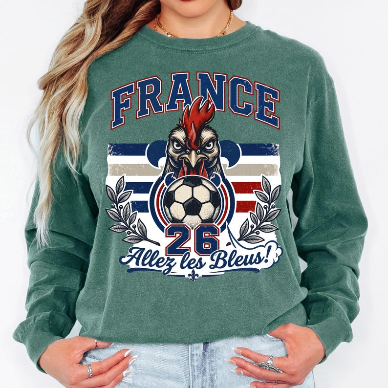 May include: Green long-sleeve sweatshirt with a graphic featuring a rooster, soccer ball, and the text "FRANCE" in blue and red. The design includes the text "26" and "Allez les Bleus!"