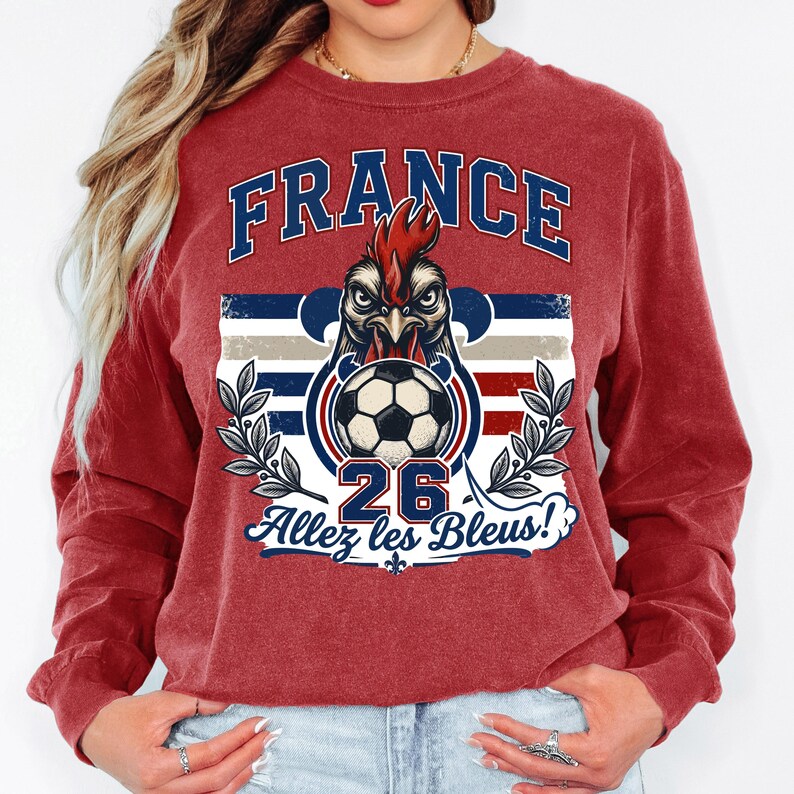 May include: A maroon long-sleeve sweatshirt featuring a graphic design. The design includes the word "FRANCE" in blue, a rooster with a soccer ball, the number "26", and the phrase "Allez les Bleus!"