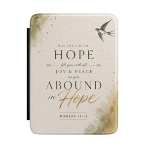 May include: A rectangular e-reader cover with a textured cream background featuring a watercolour-style olive green wash. It displays a flying bird and the text: MAY THE GOD OF HOPE fill you with all JOY & PEACE as you ABOUND in Hope ROMANS 15:13.