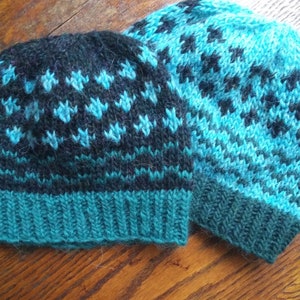 May include: Two knitted hats with a black and teal geometric pattern. The hats are made of a soft, fuzzy yarn.