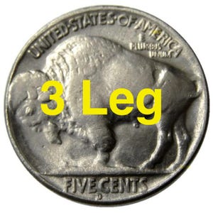 Op de afbeelding: Een zilveren Amerikaanse munt van vijf cent met de afbeelding van een buffel met slechts drie poten. De munt heeft de inscripties "United States of America" en "Five Cents".