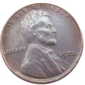 May include: A copper-coloured 1922 Lincoln cent coin. The obverse features a profile of Abraham Lincoln, the word "LIBERTY", and the date "1922". The coin also has the words "IN GOD WE TRUST".