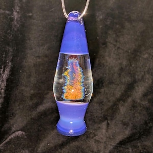 May include: A blue and clear glass pendant necklace with a lava lamp design. The pendant has a blue top and base, with a clear center containing a colorful, abstract design in orange, yellow, and blue. The necklace has a silver chain.