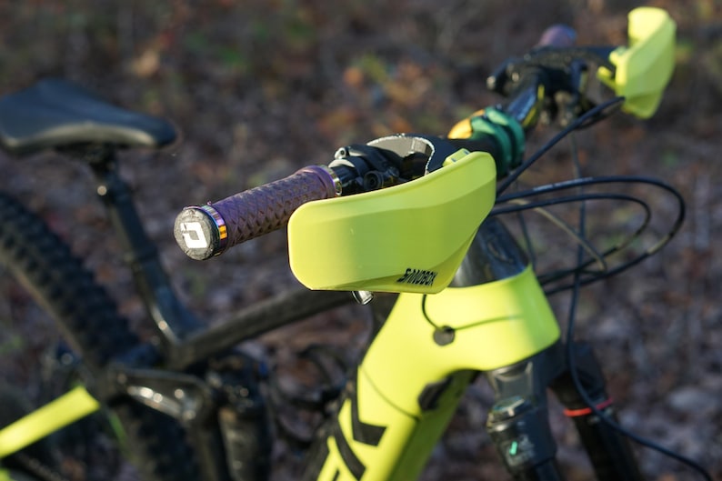 Puede incluir: Primer plano de un manillar de bicicleta de monta&ntilde;a amarillo con una empu&ntilde;adura p&uacute;rpura y negra y protectores de manillar amarillos. Los protectores tienen la palabra "Shimano" impresa en ellos.