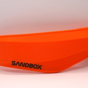 Puede incluir: Guardabarros de motocicleta de pl&aacute;stico naranja con la palabra "SANDBOX" impresa en &eacute;l.