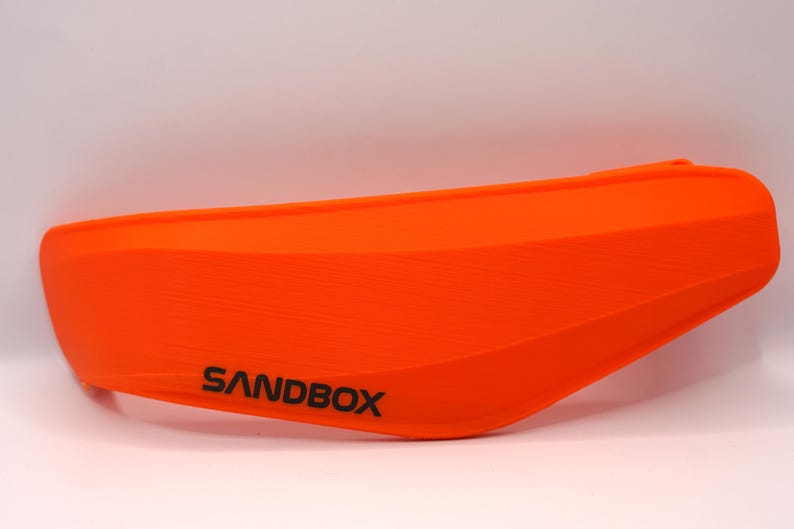 Puede incluir: Guardabarros de motocicleta de pl&aacute;stico naranja con la palabra "SANDBOX" impresa en &eacute;l.