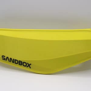 Puede incluir: Un casco amarillo brillante con la palabra "SANDBOX" impresa en negro en el lateral.