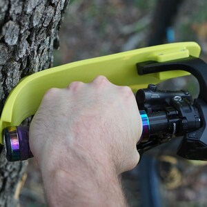 Puede incluir: Un soporte de manillar de bicicleta amarillo fijado a un tronco de &aacute;rbol. El soporte tiene un brazo negro y una palanca negra. El manillar de la bicicleta es negro con una empu&ntilde;adura de arco&iacute;ris.