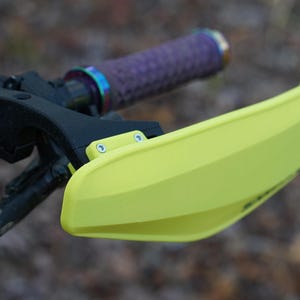 Puede incluir: Un protector de manillar amarillo brillante para una bicicleta, con dos peque&ntilde;os tornillos plateados visibles en el lateral.