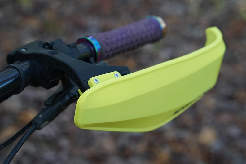Puede incluir: Un protector de manillar amarillo brillante para una bicicleta, con dos peque&ntilde;os tornillos plateados visibles en el lateral.