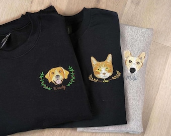 Puede incluir: Tres sudaderas negras con imágenes bordadas de mascotas. La primera sudadera tiene un labrador retriever amarillo con el nombre "Woody" bordado. La segunda sudadera tiene un gato con el nombre "Luna" bordado. La tercera sudadera tiene un perro con el nombre "Milo" bordado.