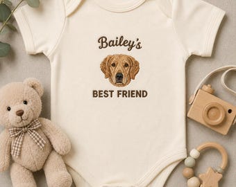 May include: A cream-coloured short-sleeve baby bodysuit featuring an embroidered golden retriever face centred on the chest. Above the dog is the text "Bailey's" and below is the text "BEST FRIEND" in brown thread. The garment has a round neckline.