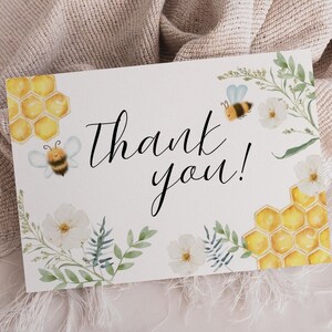 Pode incluir: Um cartão branco com as palavras "Thank you!" em escrita preta, decorado com ilustrações em aquarela de abelhas, favos de mel e elementos florais. O cartão tem uma estética suave e natural.