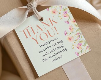 Puede incluir: Una caja de regalo envuelta con una cinta color crema y una etiqueta floral de "Gracias". La etiqueta presenta las palabras "THANK YOU!" en letras coral, un mensaje y detalles florales. La caja de regalo está envuelta en papel marrón.
