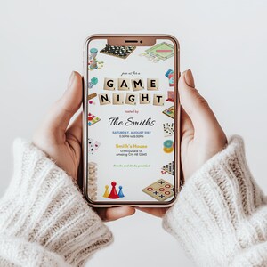 May include: A smartphone displays a game night invitation. The invitation features the words "GAME NIGHT" in Scrabble tiles, hosted by "The Smiths." Various game pieces and graphics surround the text, including dice, cards, and board games. The date and time are also included.