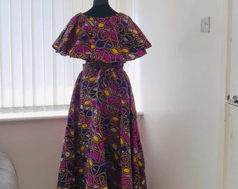 May include: A vibrant, patterned dress displayed on a mannequin. The dress features a top with a ruffled neckline and a full, flowing skirt. The fabric is a mix of purple, pink, yellow, and blue geometric shapes, creating a bold and eye-catching design.