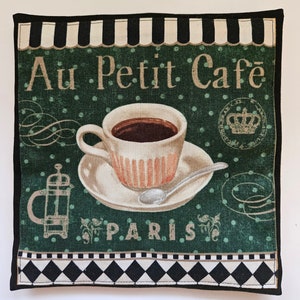 May include: A green and white fabric coaster with a black and white checkered border. The coaster features a cup of coffee, a teapot, and the text "Au Petit Cafe Paris".