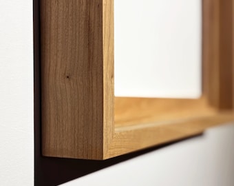 May include: Close-up of a rectangular wooden frame, showcasing the natural grain and warm tones of the wood. The frame is mounted on a white wall, with a shadow cast below. The design is simple and modern, suitable for displaying art or photos.
