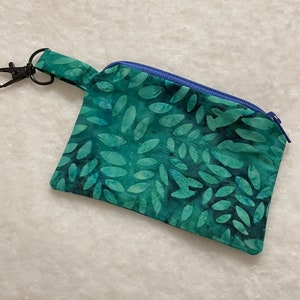 May include: A small green zippered pouch with a blue zipper and a black metal key ring. The pouch has a leaf pattern.