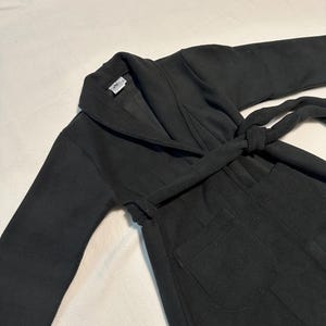 May include: A black robe with a shawl collar and a matching belt tied at the waist. The robe has long sleeves and two front pockets. The fabric appears to be a soft, medium-weight material.