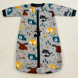 May include: A grey fleece sleep sack with a zip closure. The sleep sack has a woodland animal print featuring bears, foxes, raccoons and moose. The sleep sack has a green trim around the neck and sleeves.
