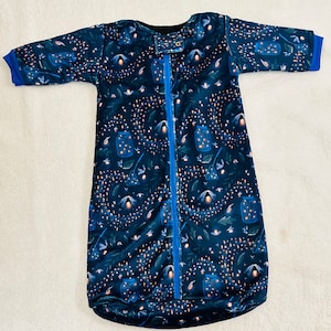 Puede incluir: Un saco de dormir azul y negro con cierre de cremallera y un patrón de luciérnagas. El saco de dormir tiene mangas largas y una capucha.