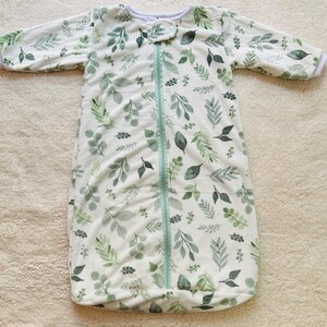 May include: White sleep sack with a zipper closure and a green leafy pattern.